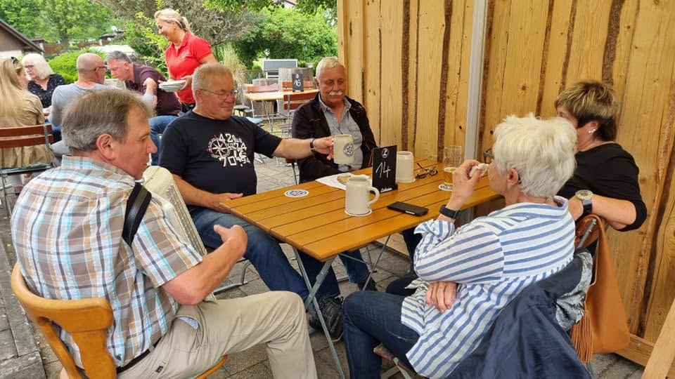 Gäste mit Bierkrügen an einem Tisch vor Holzwand